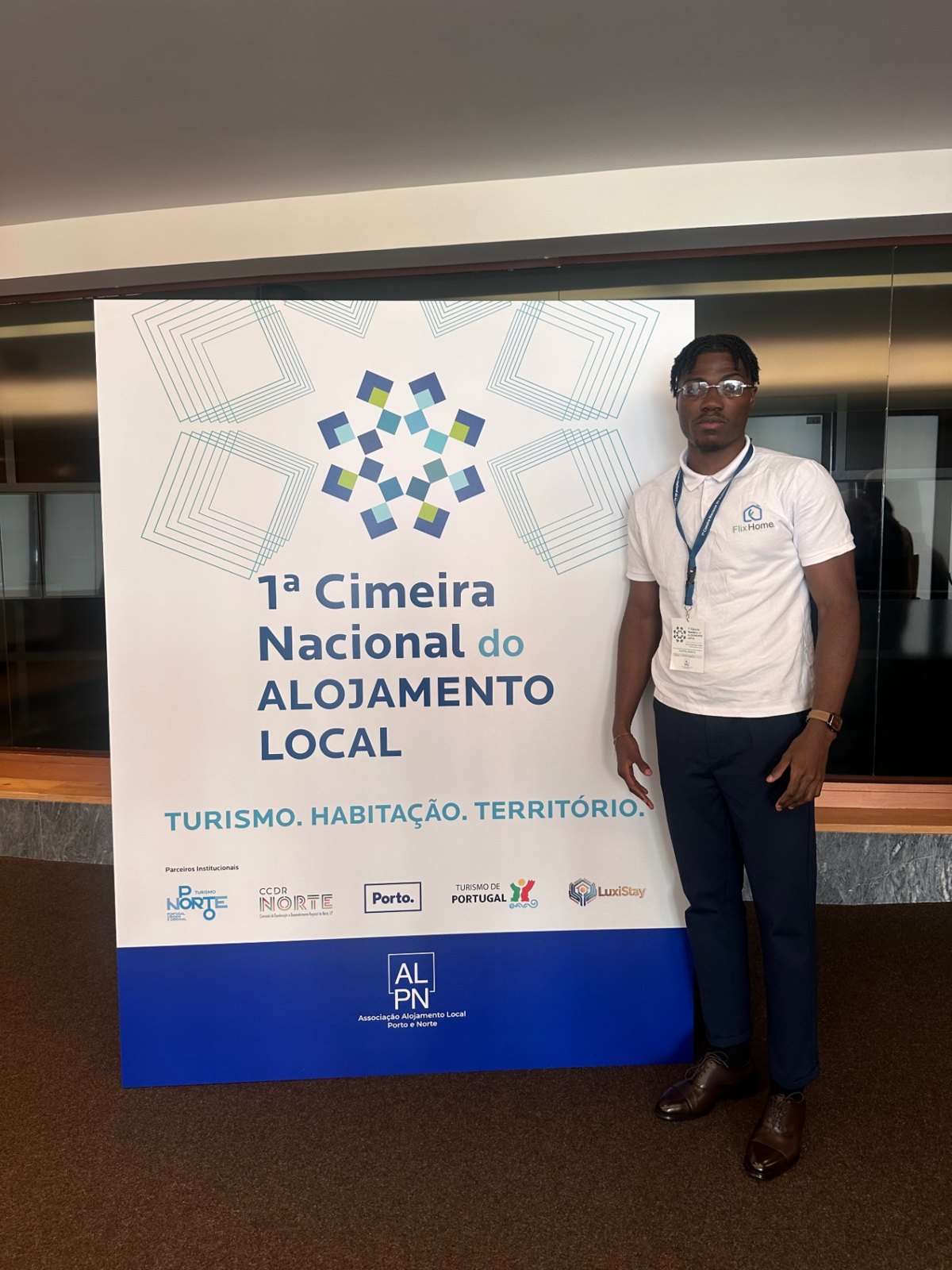 Elio Fernandes (Mvuemba Fernando Bemvindo, mvfernando), from Flix Home, beside the banner for the first National Short-Term Rental Summit in Porto